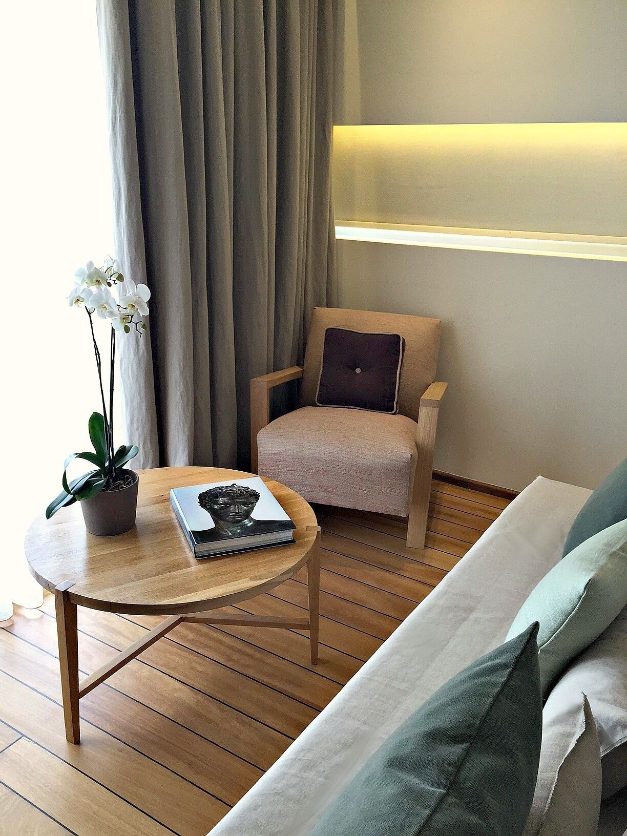 Una sala de estar moderna con piso de madera, una mesa de centro redonda, un sofá, una silla y una planta en maceta.