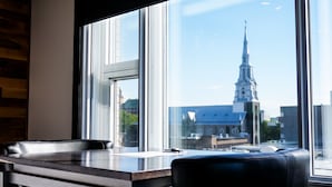 A modern office chair and desk by a large window with a view of a church spire. - Hotel Le Saint Germain (Rimouski)