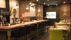 A restaurant with a long bar, multiple seating areas, and a projection screen on the wall. - Hotel Le Saint Germain (Rimouski)