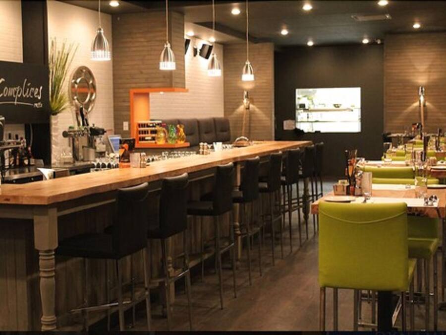 A restaurant with a long bar, multiple seating areas, and a projection screen on the wall.