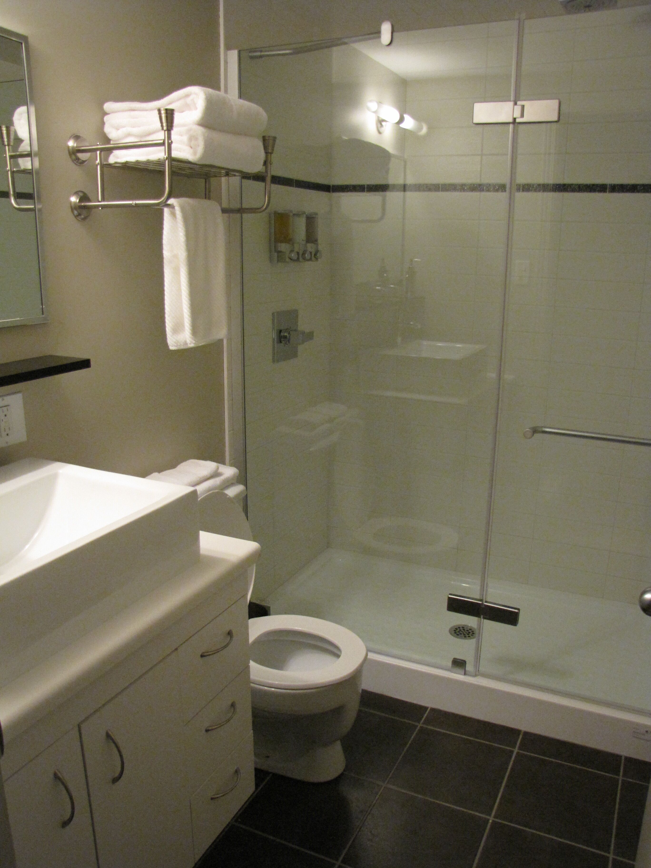 Ein modernes Badezimmer mit einer gläsernen Duschkabine, einer weißen Toilette und einem Waschtisch mit Spiegel und Handtuchhalter.