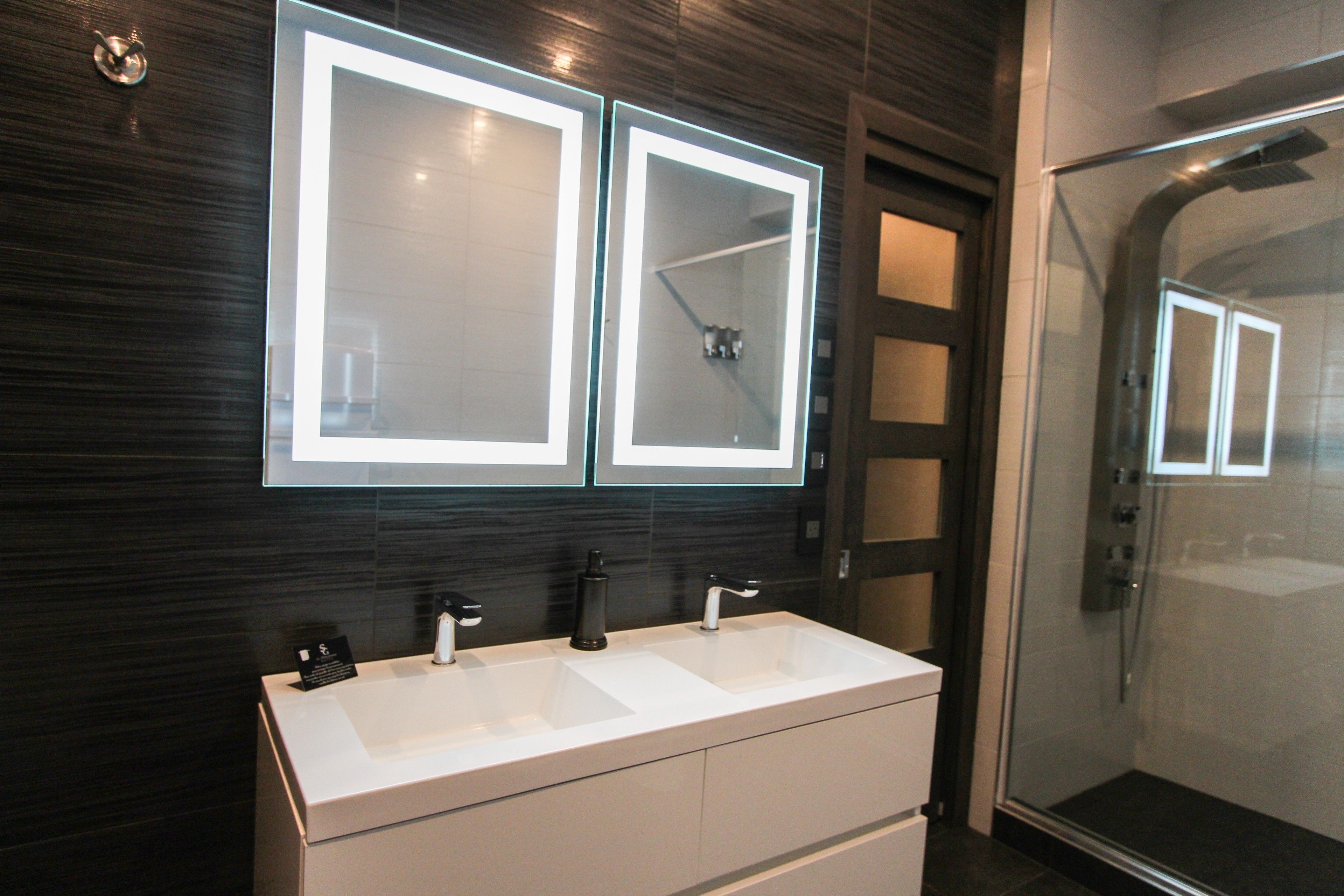A modern bathroom with two large mirrors, a double sink, and a glass-enclosed shower.