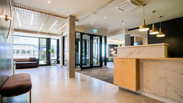 A modern lobby with a reception desk, seating area, and glass doors leading to other rooms. - Hotel Le Saint Germain (Rimouski)