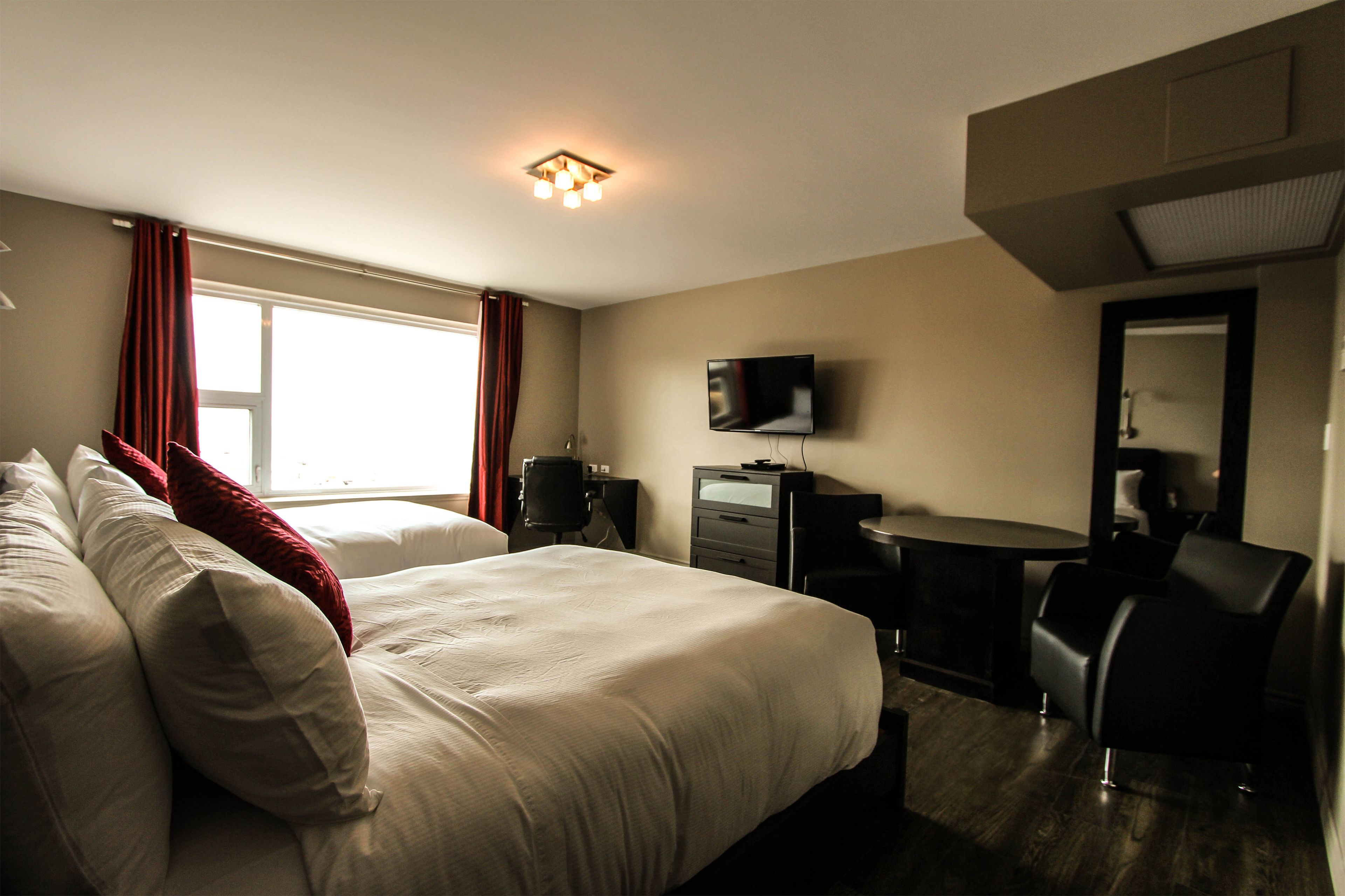 Una habitación de hotel con cama, escritorio, silla, televisión y ventana con cortinas.