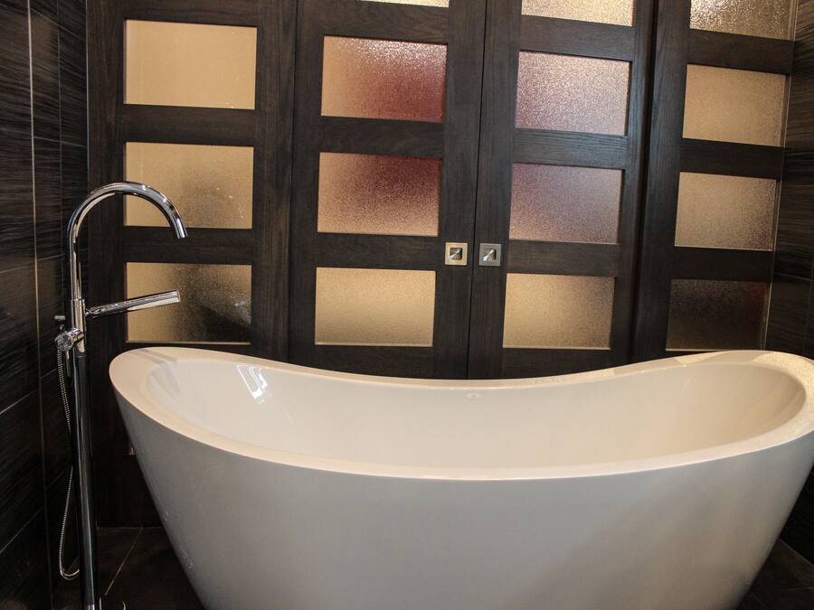Ein modernes Badezimmer mit einer freistehenden Badewanne, einer Dusche und dunklen Fliesenwänden.