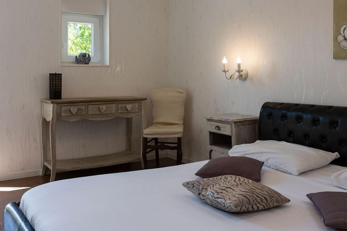 Une chambre à coucher comprenant un lit, un bureau, une chaise, une table de chevet et un luminaire fixé au mur.