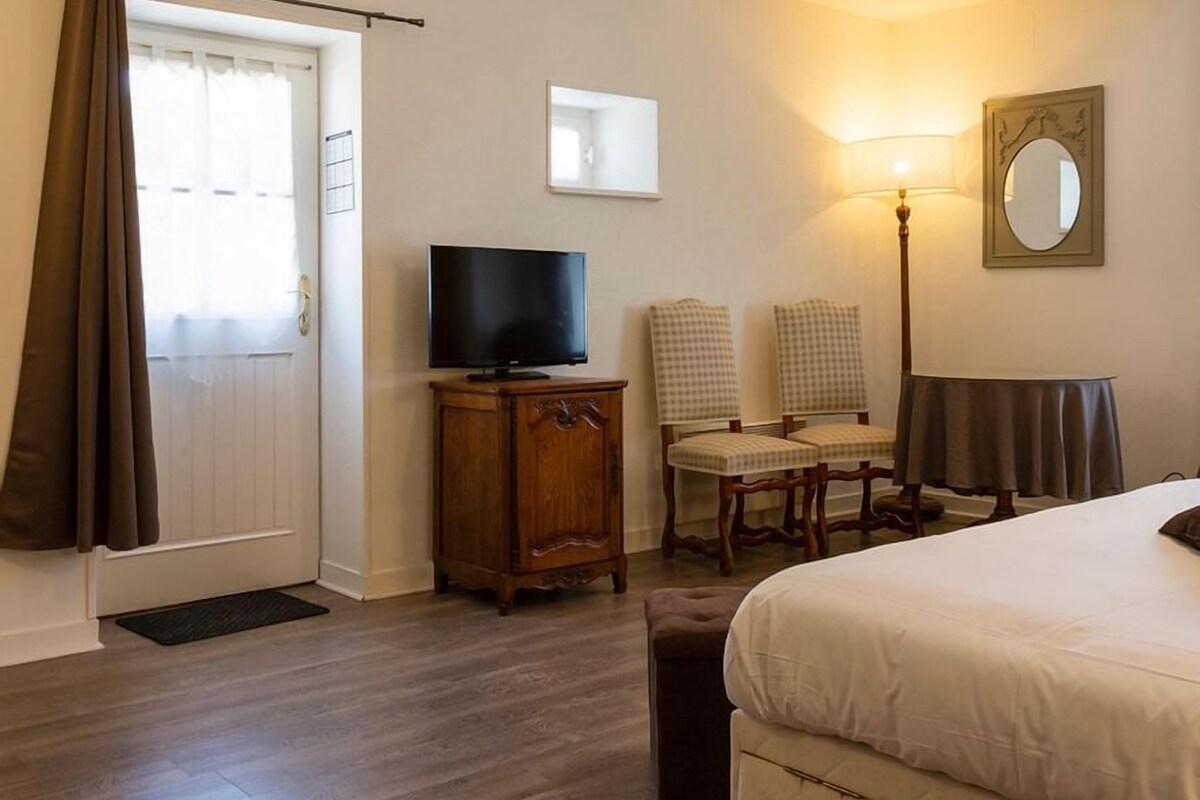 Habitación de hotel con cama, televisor, escritorio, dos sillas, lámpara y espejo.