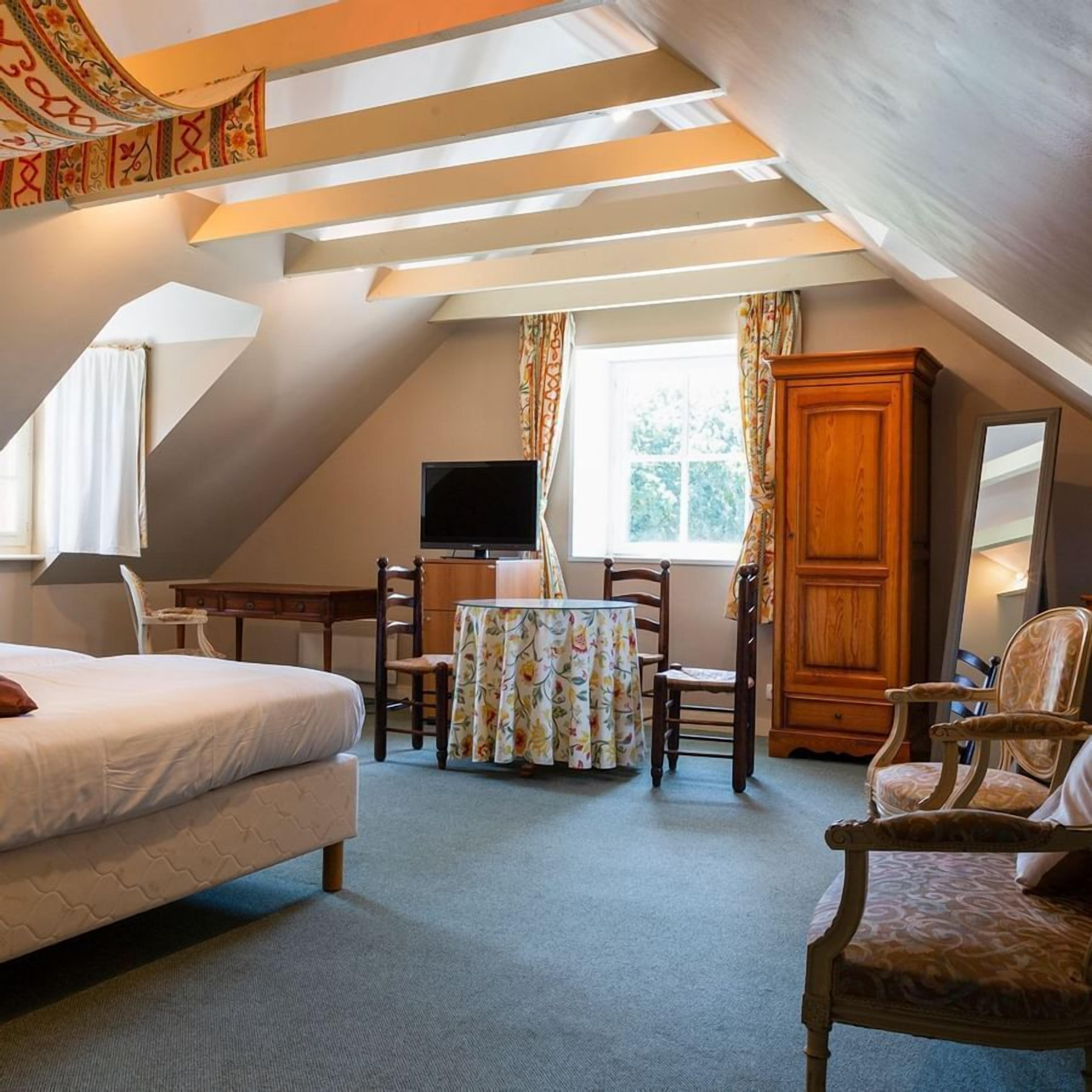 A bedroom with a bed, a desk, a chair, a television, and a window.