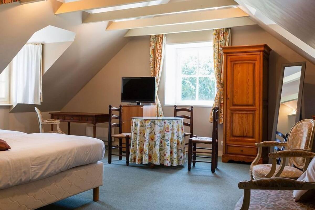 A bedroom with a bed, a desk, a chair, a television, and a window.