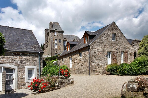 A stone building with a gravel driveway and red flowers in the foreground.