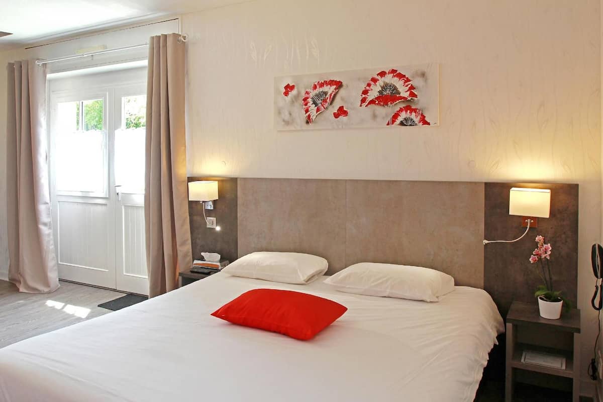 A hotel room with a large bed, two bedside lamps, a wall-mounted artwork, and a sliding door to the left.
