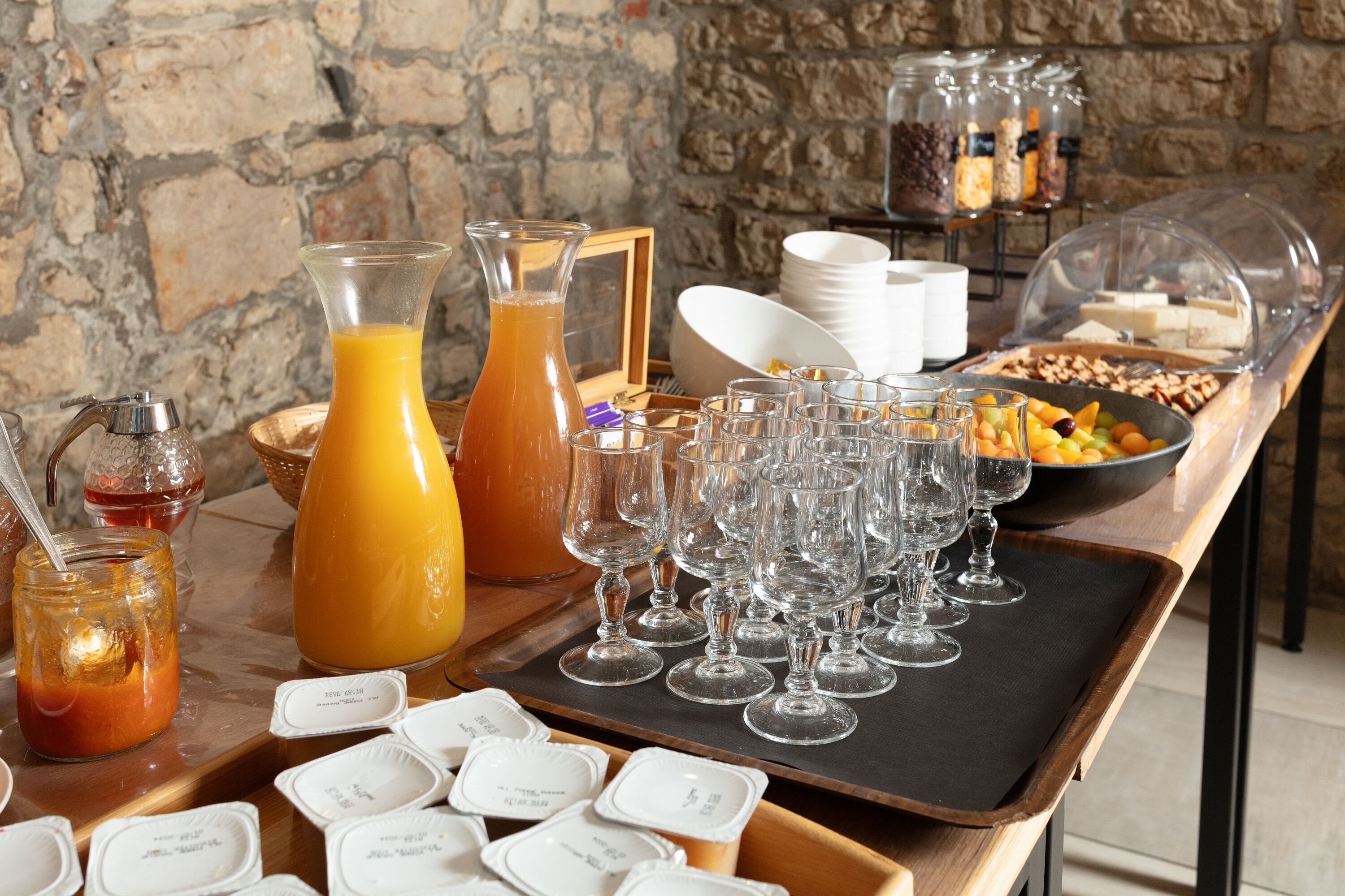 Um buffet de café da manhã com diversos alimentos, uma seleção de copos e um fundo de parede de pedra.