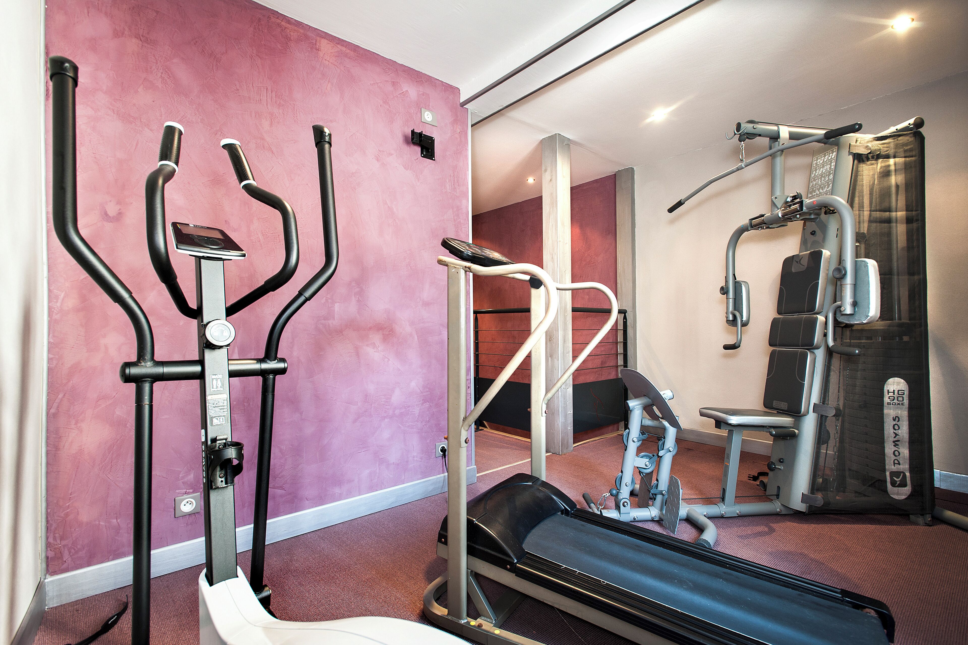 Une salle de sport équipée de matériel d’exercice, notamment un tapis de course, des appareils de musculation et un vélo d’appartement.
