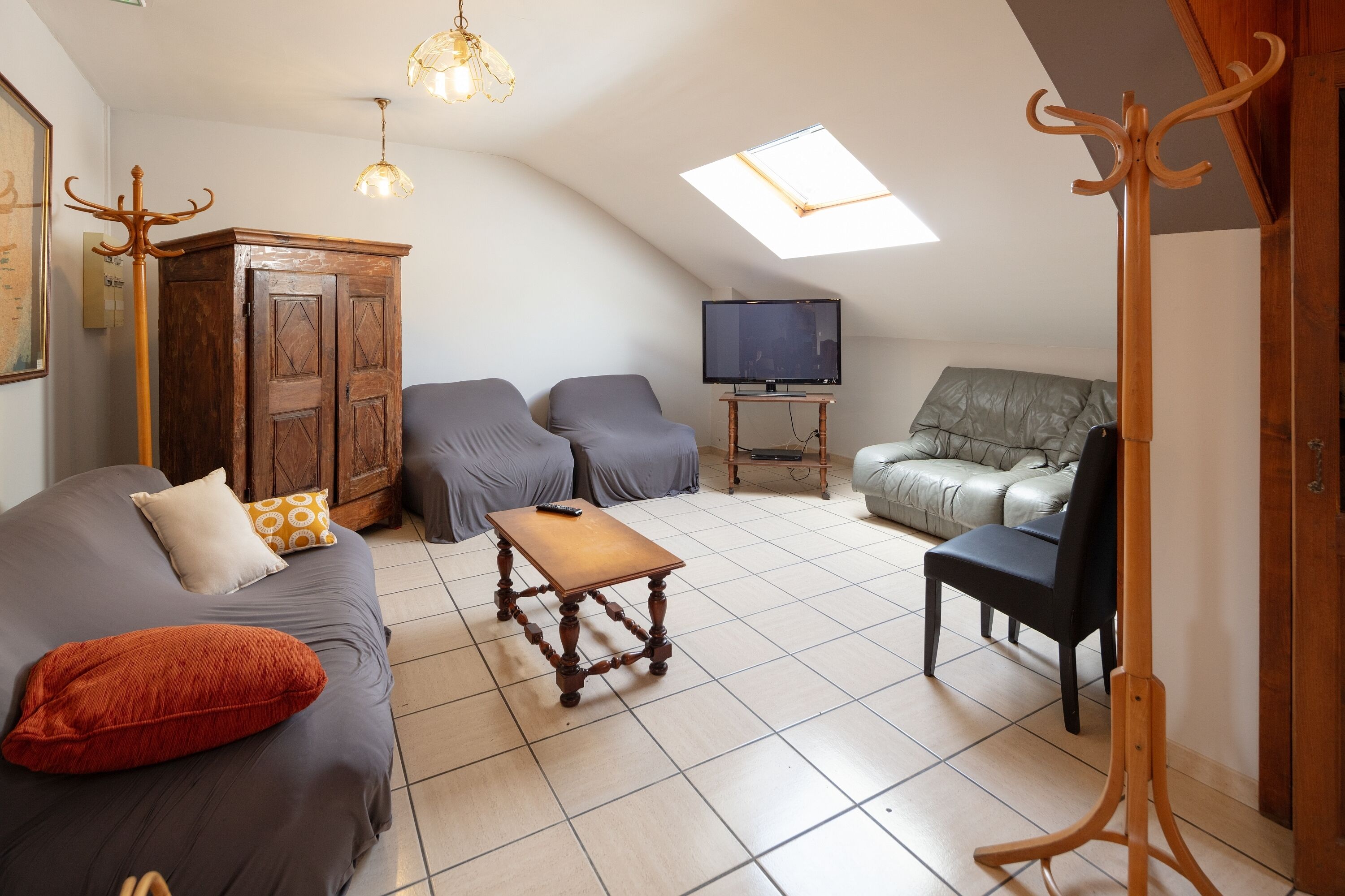 Un salón estilo loft con techo alto, un armario de madera, un sofá, una mesa de centro, un televisor sobre un pedestal y un sofá gris.