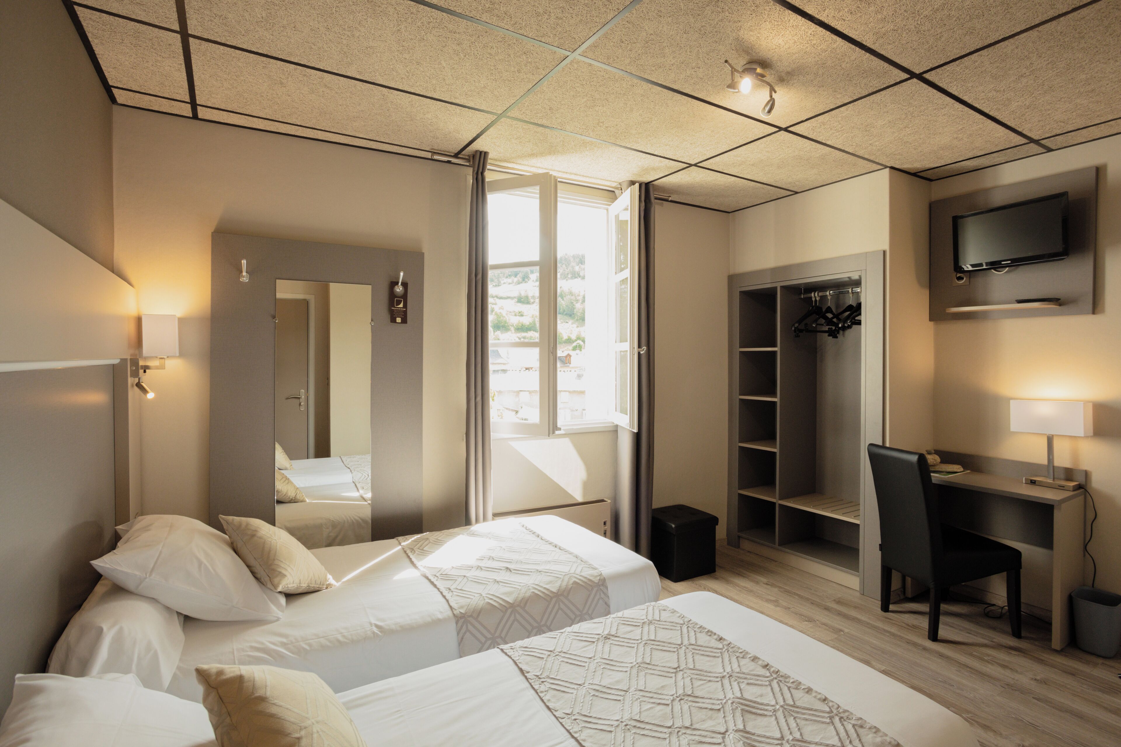 A hotel room with two beds, a desk, a TV, and a wardrobe.