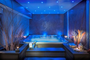 A modern spa room with a hot tub, blue ambient lighting, and decorative plants. - Hotel Family and Spa (Meyrueis)