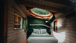 Un dormitorio de cabaña de madera con tragaluz, una cama con almohadas y una mesita de noche.