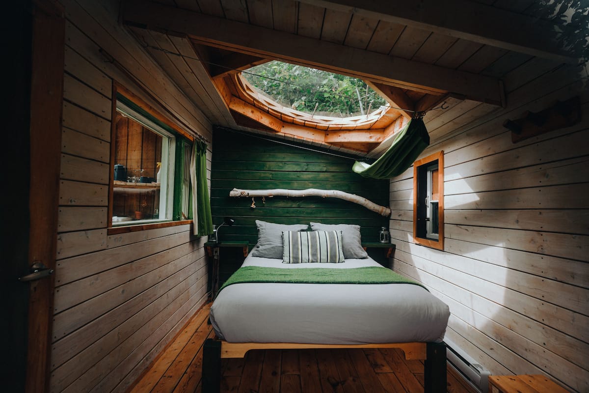 A wooden cabin bedroom with a skylight, a bed with pillows, and a nightstand.