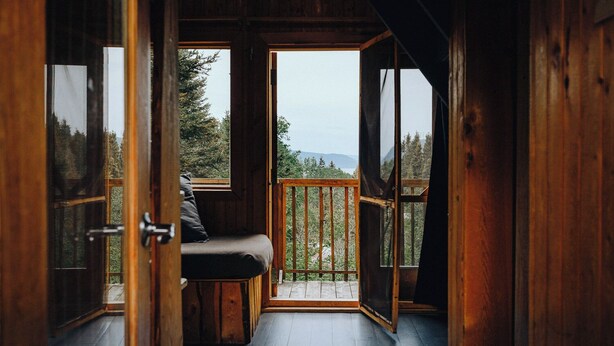Una cabaña de madera con un banco y vistas al bosque.
