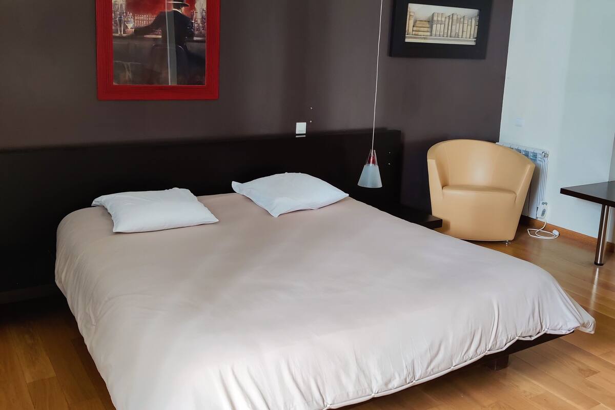 A modern bedroom with a large bed, a chair, and two framed pictures on the wall.