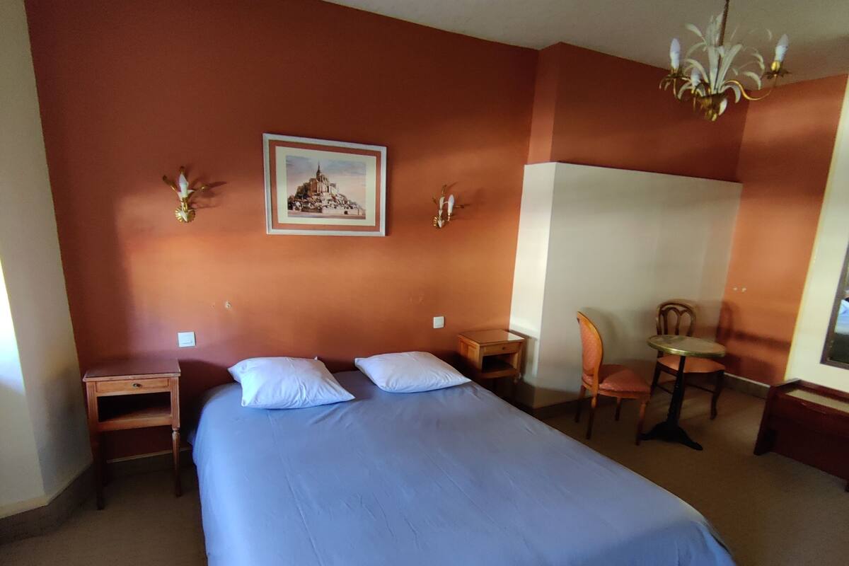 A hotel room with a large bed, a desk, a chair, and a small table.