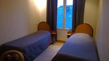 Et lille hotelværelse med to senge, et vindue med gardiner og havudsigt.