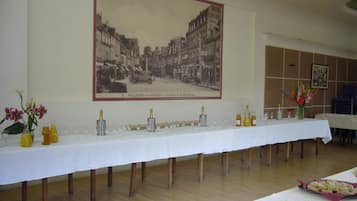 Une longue table de banquet, dressée avec des flûtes à champagne, des verres et des compositions florales, et une affiche représentant une scène de rue d’époque accrochée au mur.