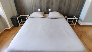 Een bed met een houten hoofdbord, twee nachtkastjes en een lichtgekleurde muur.