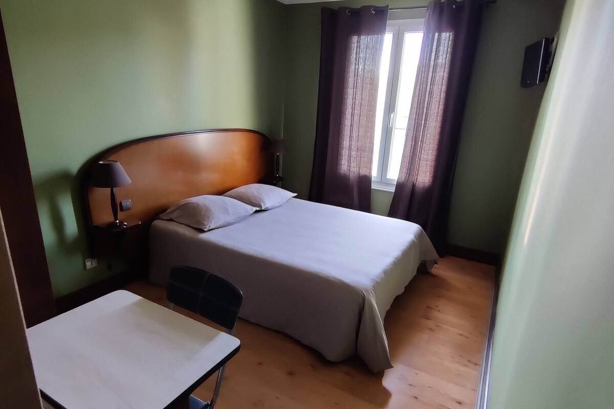 A hotel room with a bed, a desk, a chair, and a ceiling fan.
