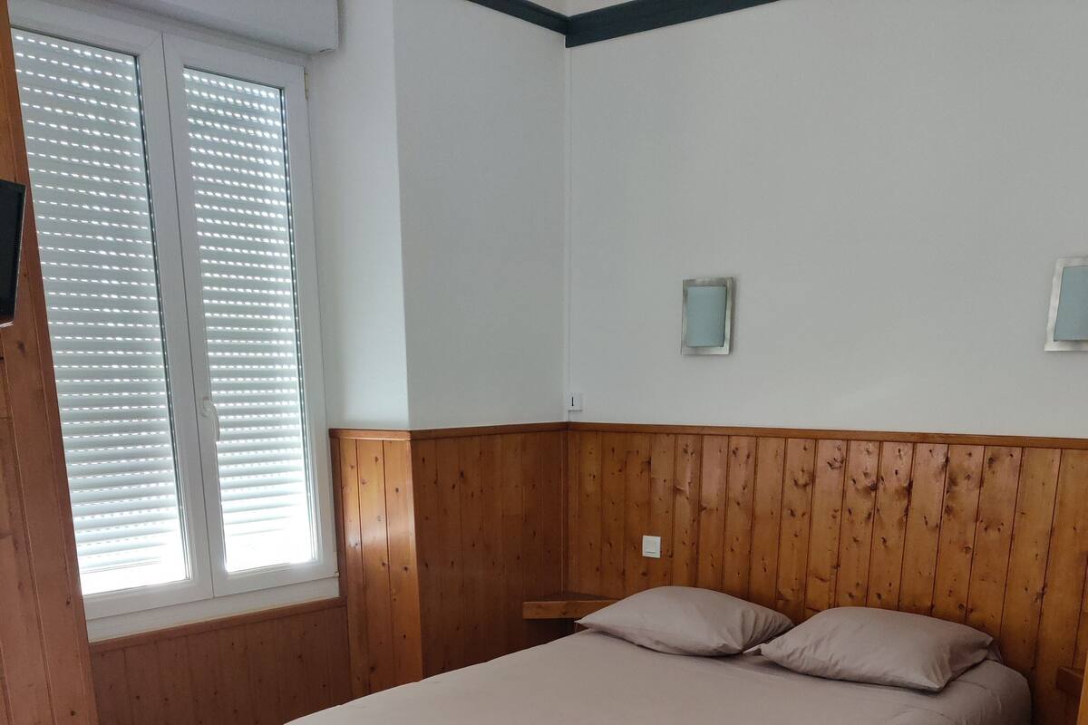 A bedroom with a wooden headboard, a bed with beige bedding, a nightstand, and a window with blinds.