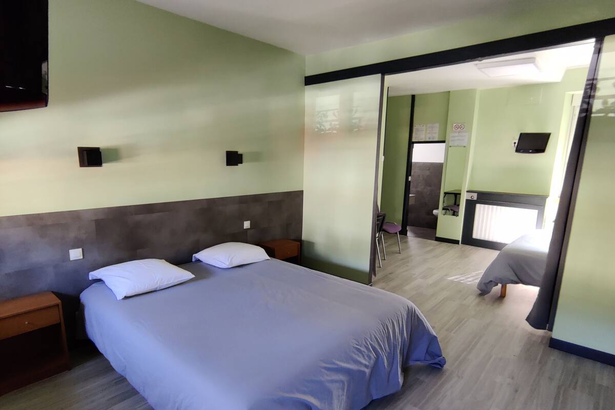 A hotel room with a large bed, a small bedside table, a mirror, and a sliding door leading to a bathroom.