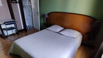 Ett hotellrum med en säng, ett nattduksbord, en lampa, ett trägolv och ett badrum som syns genom en öppen dörr.