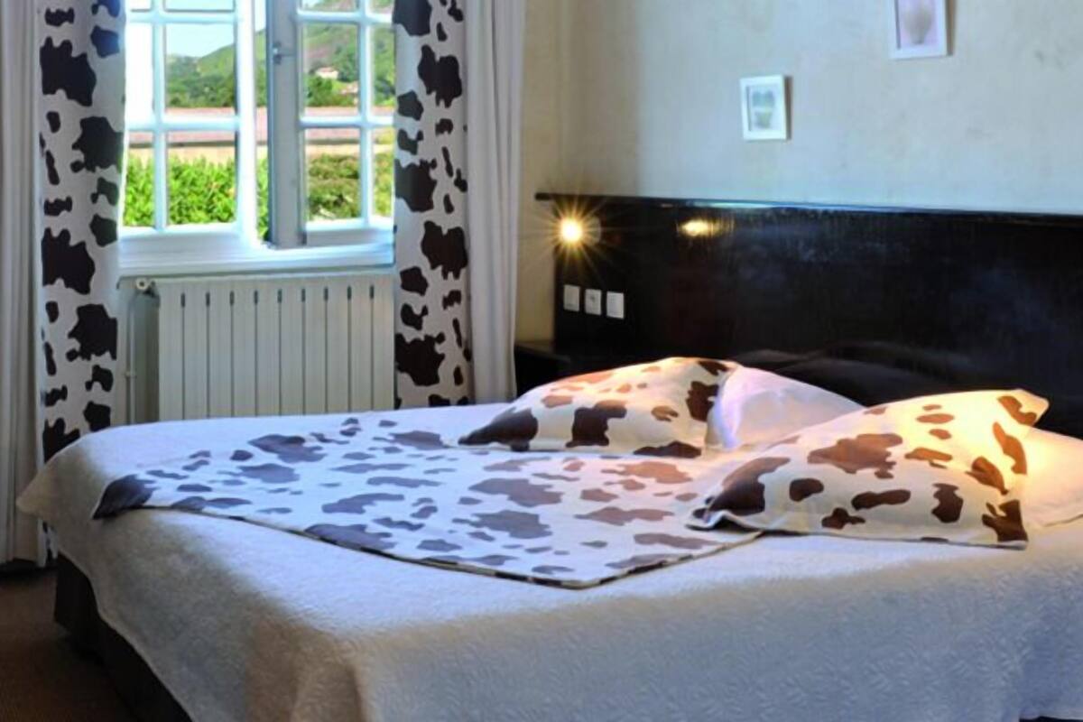 A hotel room with a bed featuring a cow print bedspread, a window with curtains, and a headboard with a light fixture.