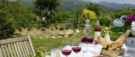A table set outdoors with wine glasses, a bottle of wine, bread, and a basket of bread.