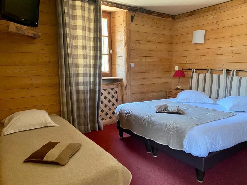 A wooden room with a bed, a bench, a small table, and a TV.
