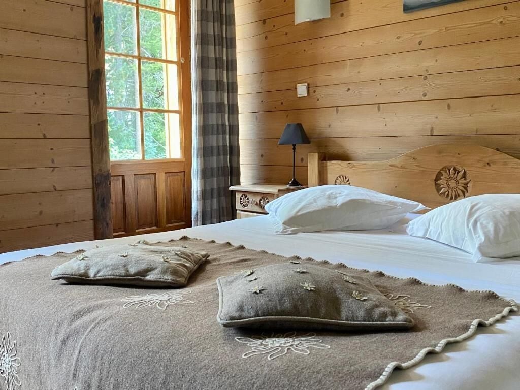 Een houten slaapkamer met een bed, kussens, een nachtkastje en een raam.