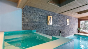 Un área de spa con pared de piedra, bañera de hidromasaje y piscina.