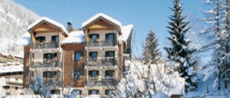 Ein mehrgeschossiges Gebäude mit einer symmetrischen Fassade, großen Fenstern und einem mit Schnee bedeckten Dach.