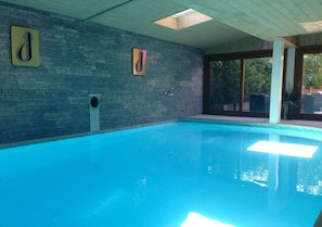 Uma piscina interior com parede de tijolos, corrimão e janela.