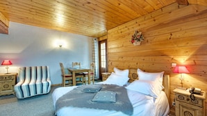 Una habitación con paneles de madera, una cama, dos mesitas de noche, una silla, una mesa y una lámpara.