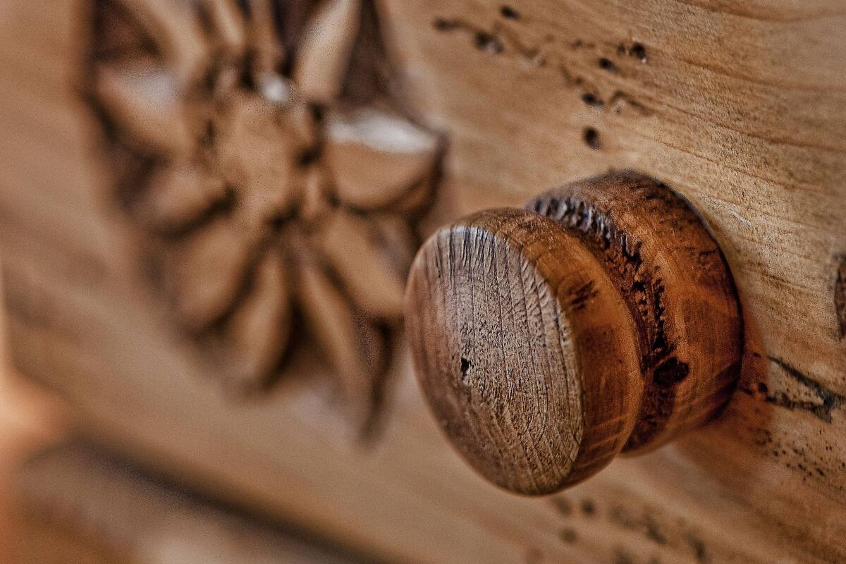 Close-up de uma gaveta de madeira com um desenho floral entalhado e um puxador redondo.