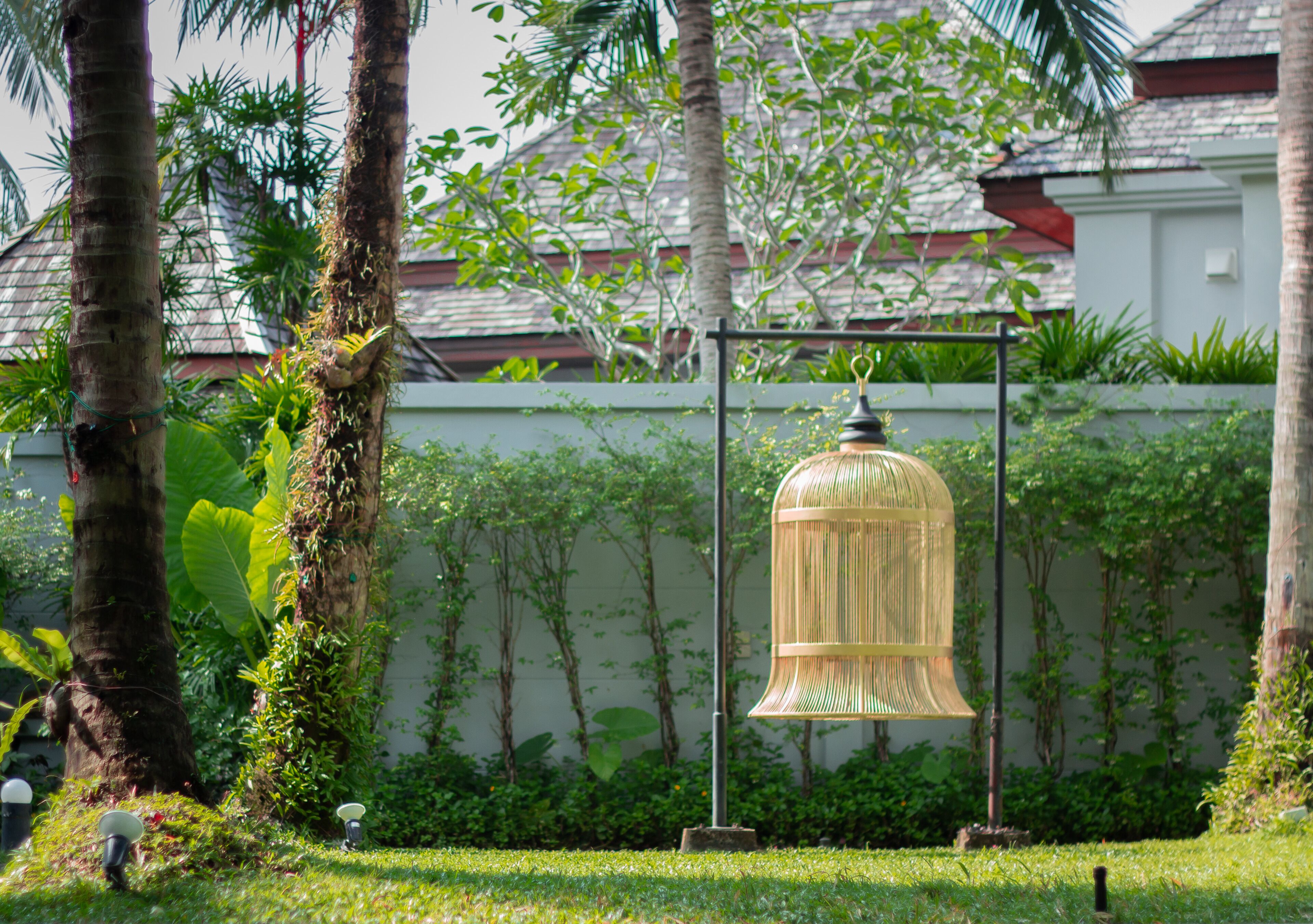 A garden with a decorative metal structure, lush greenery, and a building with a tiled roof in the background.