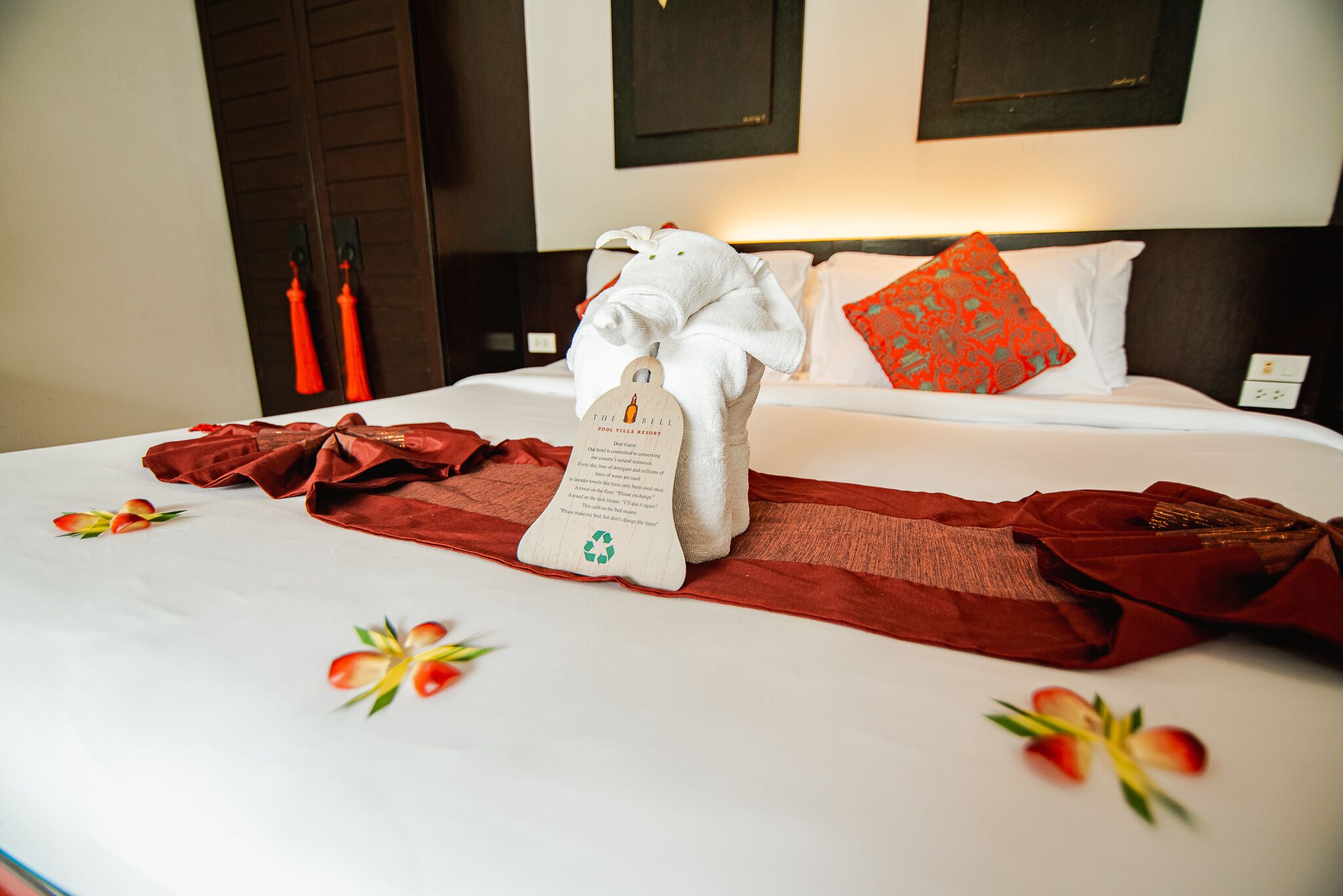 A neatly made bed with a white towel, red throw, and a tag with a recycling symbol.
