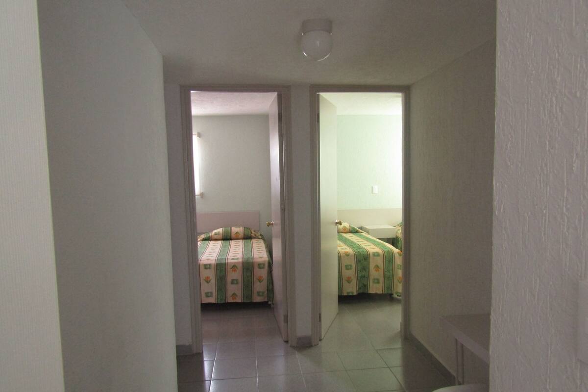 A narrow hallway leading to two small bedrooms with tiled floors and plain walls.