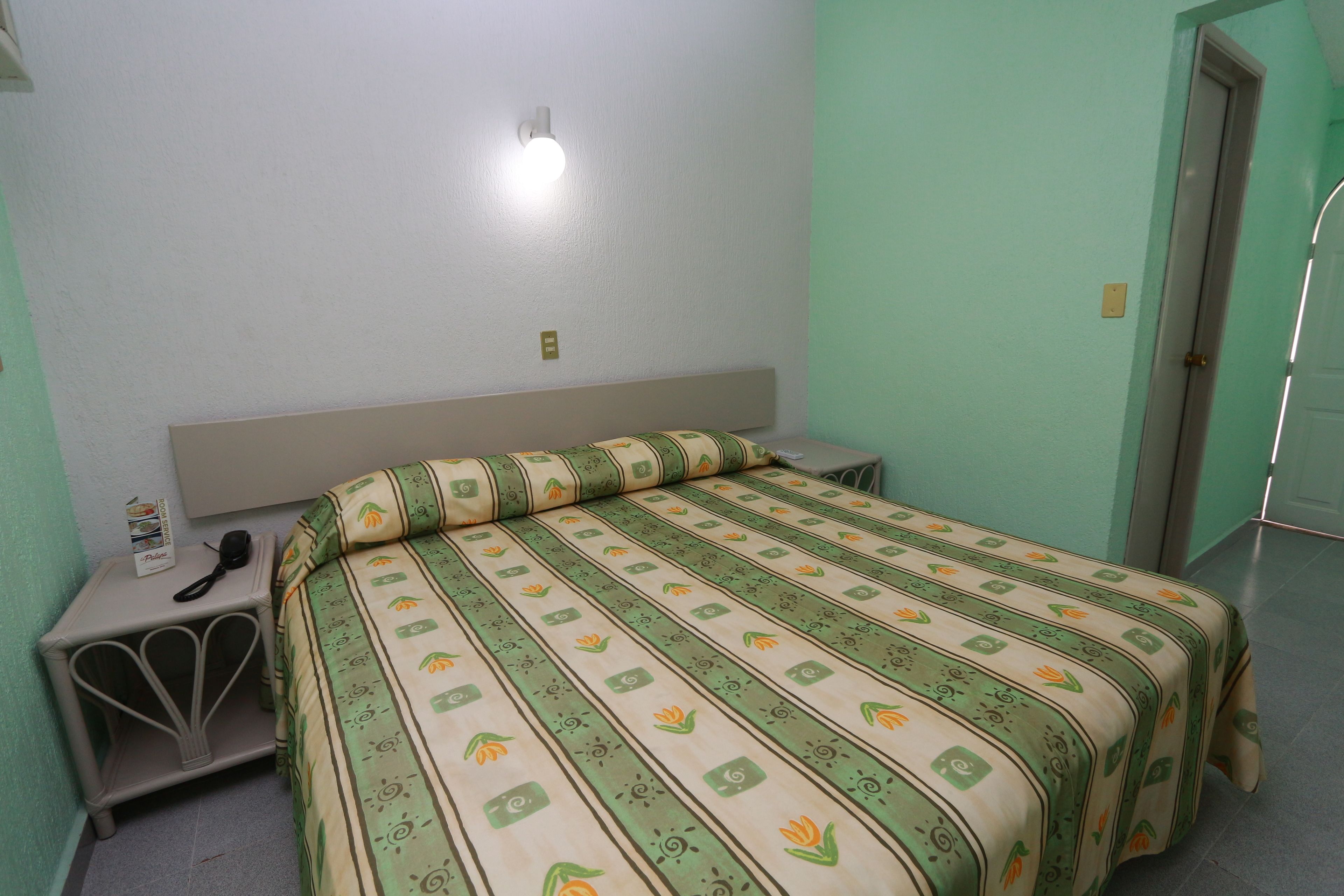 Una cama individual con una colcha estampada, una mesita de noche con teléfono y una lámpara de pared.