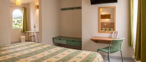 Un dormitorio con cama, escritorio, silla, televisor y ventana con cortinas.