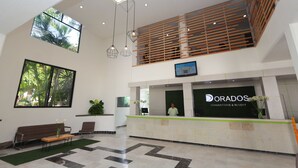 A reception area with a reception desk, a large window, a sofa, and a staircase. - Dorados Conventions & Resort (Yautepec)