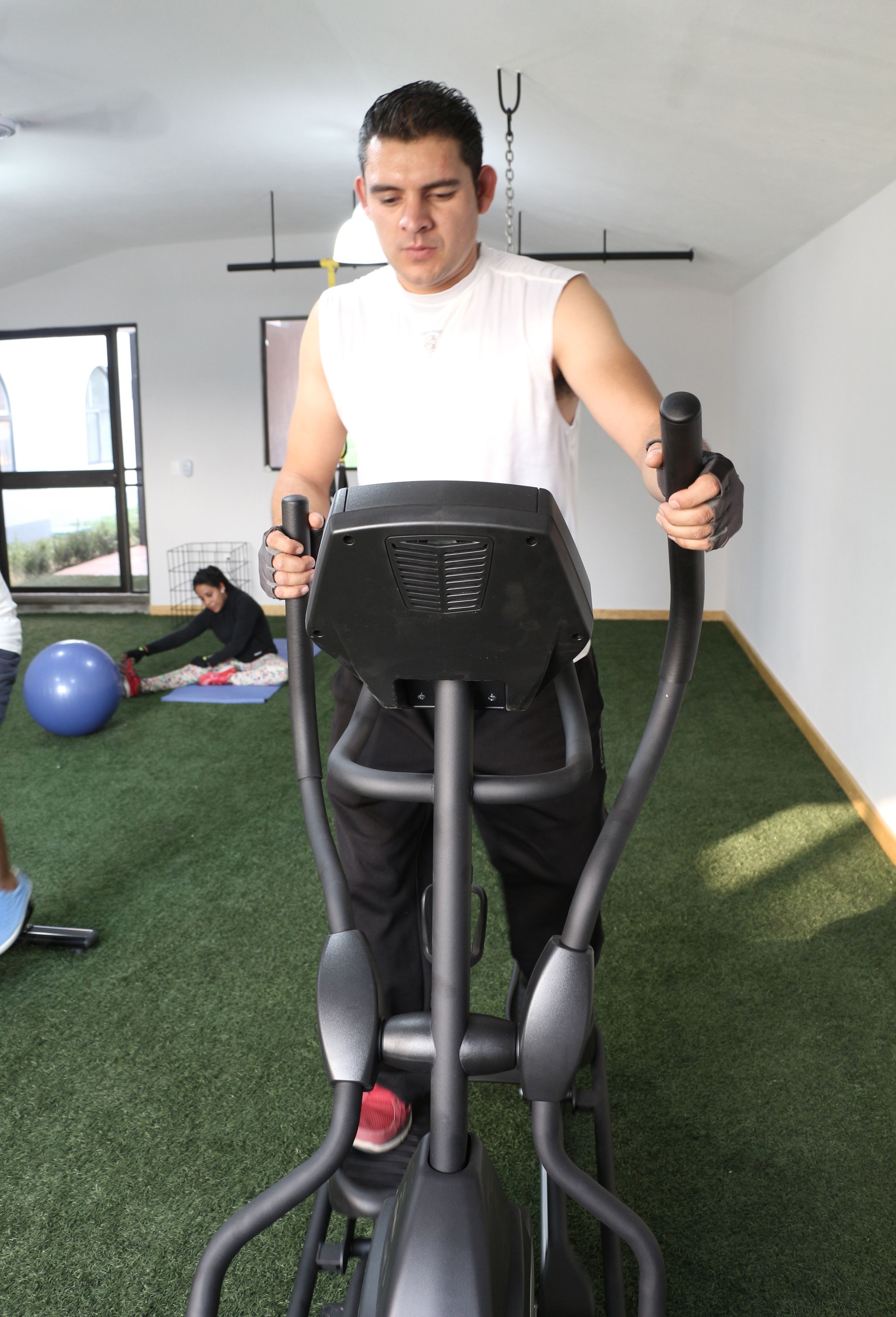 A person using an elliptical trainer in a room with green artificial turf flooring, a window, and a door in the background.