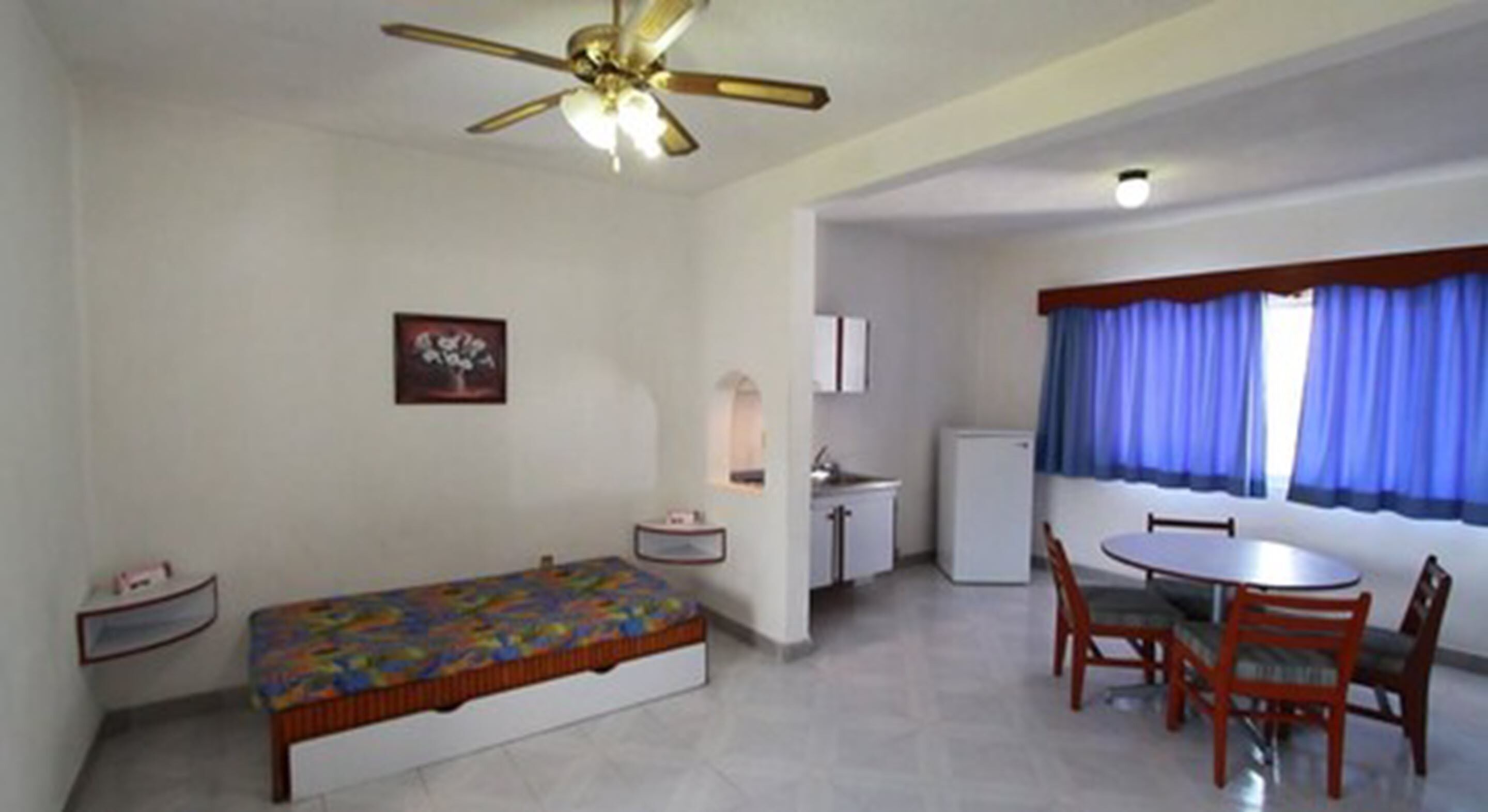 A room with a bed, a desk, a chair, a small refrigerator, and a window with curtains.