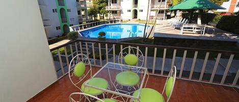 Un balcón con piscina, sillas verdes y una valla blanca.